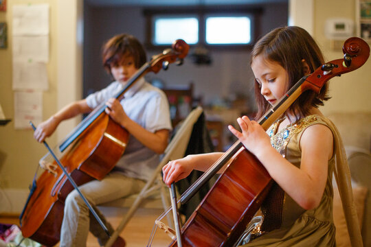 Brother and sister practicing cello together in living room