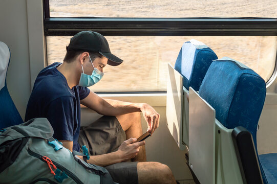 Young Man Wearing Face Mask Using Smartphone While Traveling By Train