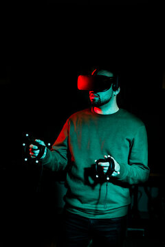 A young man wearing virtual reality glasses stands in a darkened room