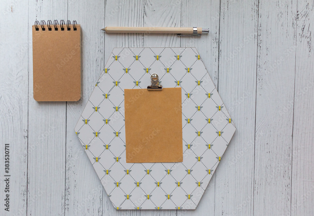 Wall mural brown blank piece of papaer on octagon shaped note board beige pencil and brown notebook white wooden background.  Bee  pattern note board. Stationery scene.