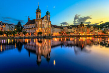 Fototapeta na wymiar Blue twilight on Lake Lucerne in Switzerland. Jesuitenkirche Church of St. Francis Xavier reflects on Reuss river of Lucerne town. Reflections of Lucerne cathedral on the river at night.