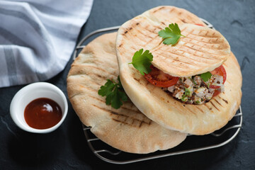 Grilled pitas stuffed with doner meat and vegetables on a metal cooling rack, horizontal shot on a black stone background