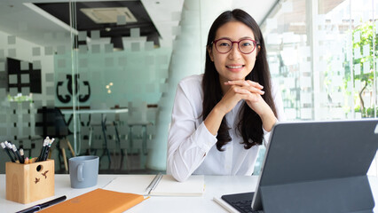 Cropped shot of female office worker smiling and looking into camera while working with tablet in...
