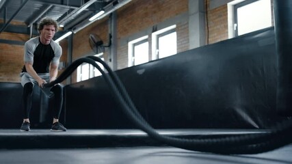 Anxious kickboxer training with ropes in sport club. Fighter using ropes at gym