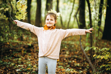 Little girl with maple leaves in hand in a sunny forest having fun. Autumn weekend in the woods