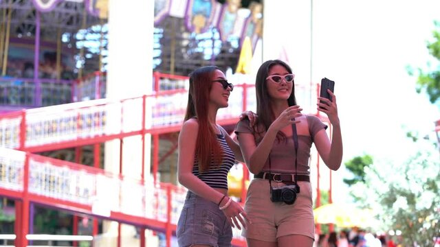 Two young Asian women taking pictures with mobile phones in an amusement park.