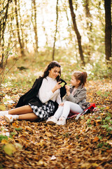 Fototapeta premium Autumn weekend in the forest mood. The sisters sit on a yellow leaf in the sunny forest and have fun