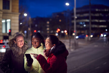 Group Of Female Friends On City Street At Night Ordering Taxi Using Mobile Phone App