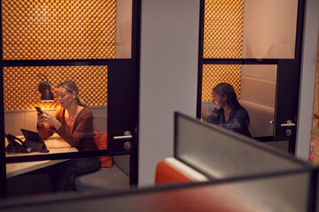 Businesswomen Working Late In Individual Office Cubicles Using Laptop And Digital Tablet