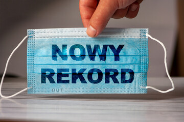 hand holds a medical and protective mask with the polish word nowy rekord (english = new infection...