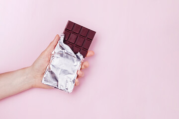 Hand holds dark chocolate bar in foil.