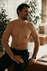 Obraz premium European man in his flat. Sitting in the living room. Bronze skin. Dark eyes and hair. Beard. Light colored interior. Casual clothes style. Weekend at home. Domestic atmosphere. Cosiness and comfort