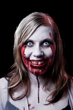 Dark studio photo of a female zombie or vampire with blonde hair on black background.