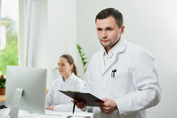Fototapeta premium A serious surgeon with bristles holds a black clipboard with documents.