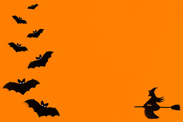Fototapeta na wymiar Silhouettes of a flock of bats and a witch flying on a broom made of black paper on an orange background. Halloween greeting template with copy space. Flat lay for your design. ready-made template