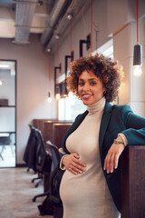 Portrait Of Pregnant Businesswoman Holding Bump Working In Modern Office