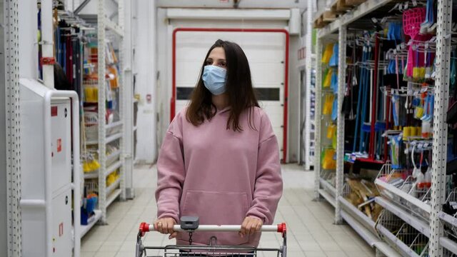 In a supermarket, a woman pushes a shopping cart through a section of household chemicals and toilet paper in a store.
