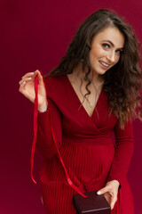 Beautiful female taking box present for Christmas and New Year holidays. Positivity woman in red dress opened box with stripe and happy smiling. Red studio background.