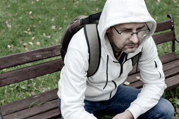 Fototapeta premium A ma in a hood sitting on a park bench