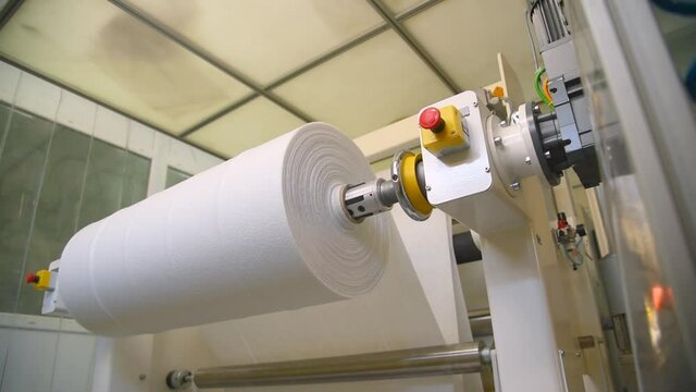 White non-woven material with nanofiber is slowly wound on a roll on the machine. The fabric is intended for making medical masks. Protection against coronavirus and Covid-19