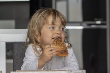 Little girl eating pizza in the kitchen, sitting at the table. Dessert for the child.