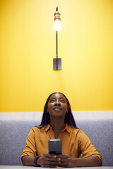 Woman With Mobile Phone Sitting Under Light Bulb In Office Suggesting Inspiration Or Idea