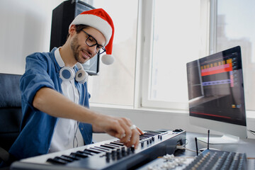 Merry Christmas and a happy new year Composer hands on piano keys in recording studio. music production technology, man in christmas hat is working on pianino and computer keyboard on desk. © Vlad