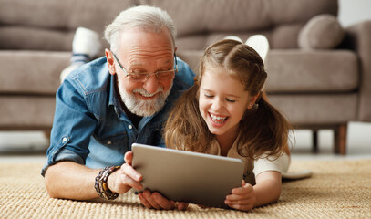 Grandfather and granddaughter using tablet on floor.