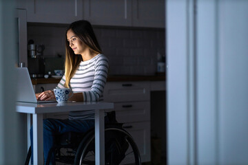 Young woman in wheelchair working on laptop till late
