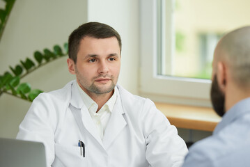 A close photo of a caucasian doctor in a white lab coat is describing the treatment to a bald male...