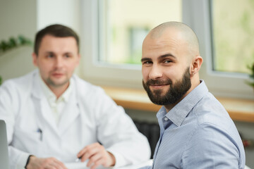 A bald male patient is smiling near a caucasian doctor in a white lab coat in a hospital. A man...