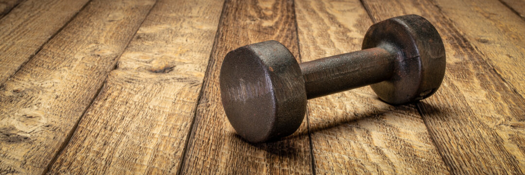 vintage rusty iron dumbbell on grained barn wood background - fitness concept web banner