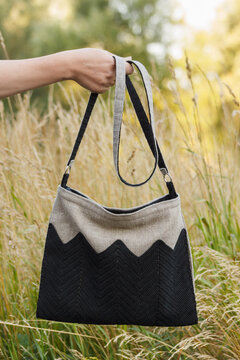 Crossbody bag in women's hands. Linen bag. Knitted black decor.