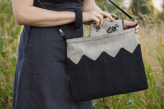 Crossbody bag in women's hands. Makeup bag and bracelet. Linen bag. Knitted black decor.