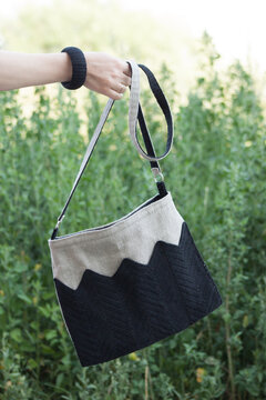 Crossbody bag in women's hands. Linen bag. Knitted black decor.