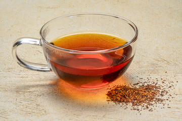 rooibos red tea  -  a glass cup of a hot drink and loose leaves, tea made from the South African red bush, naturally caffeine free