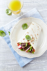 Tortilla wrap with beef meat and fresh vegetables. Rustic wooden background. Top view. Copy space.	