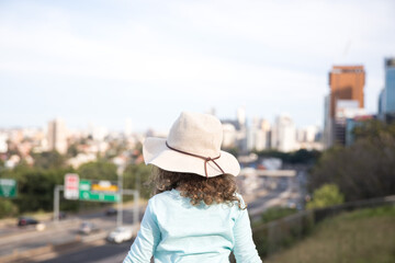 View of a young girl child from behind wearing a broad rim sun hat blue top with her arms...