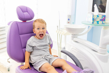 a small child two years old sitting in a lilac dental chair with his mouth open