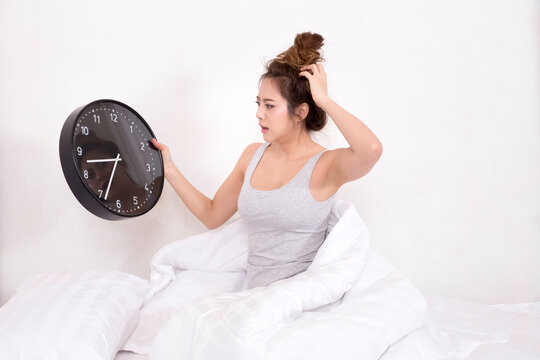 Asian Woman Too Late Wake Up Hold Big Black Clock On Bed In Bedroom At Home.