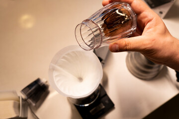 A man grinds coffee beans with a traditional coffee grinder using a hand-crank to make the coffee beans powdered and a drop of hot water into the coffee beans. 