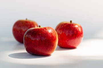 Three red apples with focus on the foreground and blur background on a white table. Selective focus
