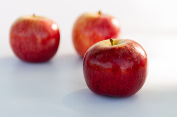 Three red apples with focus on the foreground and blur background on a white table. Selective focus
