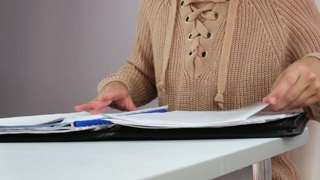 Recorded information. A woman is engaged in office work. A woman works at an offside table. the woman searches for the necessary document, parses and checks the documents.