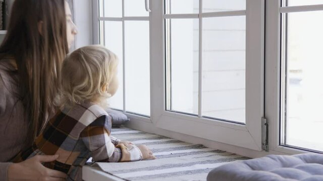Mother and little daughter having fun on Christmas morning. Precious family moment, young mom playing with her cute daughter by the white window and Christmas tree.