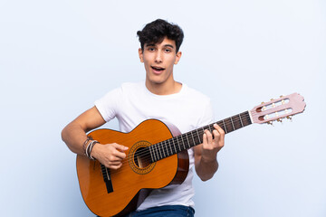 Obraz premium Young Argentinian man with guitar over isolated blue background