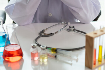 Female doctor or scientist with medical equipment composition, stethoscope, vaccine, syringe and test tube making research in clinical laboratory