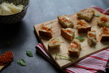 Bread cubes spread with pork lard and sprinkled with red hot ground pepper (red hot ground paprika). Served on the wooden cutting board. 