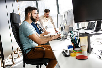 Young programmer sitting at the desk in his office and working .	
