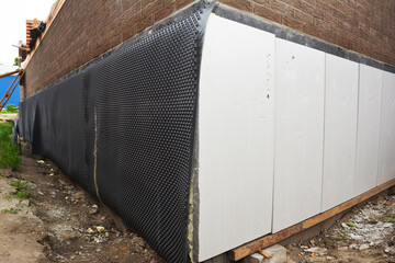 A close up on an external foundation wall of a brick house with polystyrene insulation  covered...